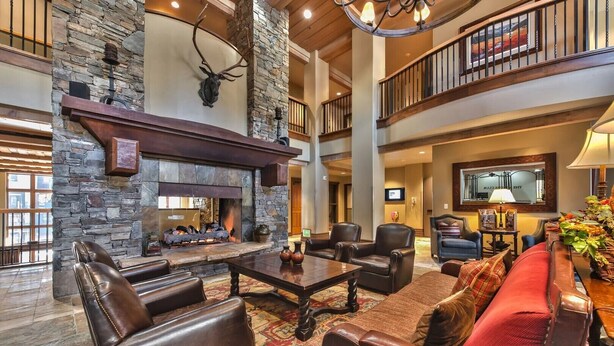 A spacious living room with a stone fireplace, leather furniture, and a high ceiling with wooden beams. - Welcome to Your 4BR/4BA Perfect Mountain Retreat in Park City (Park City)