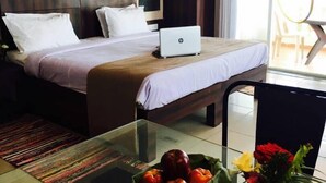 A hotel room with a bed, a laptop, a glass table with a fruit bowl, and a vase with flowers. - Presidency Highland Resort (Patan)