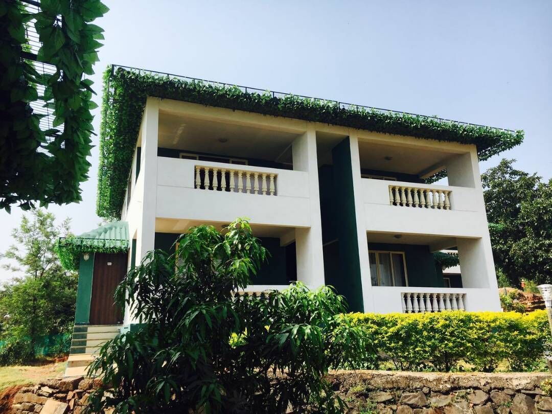 A two-story building with balconies, surrounded by greenery and a stone wall.
