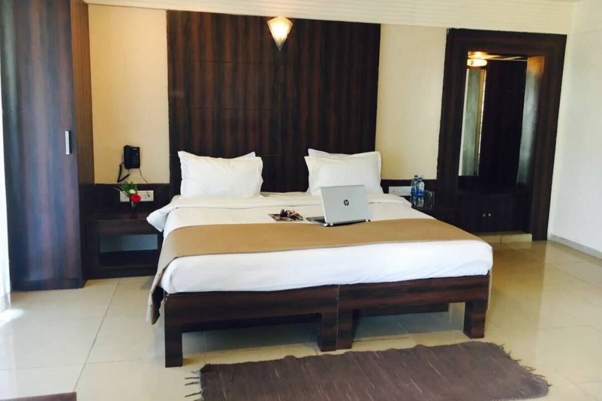 Un grand lit avec un ordinateur portable, une table de chevet avec un téléphone et un miroir.