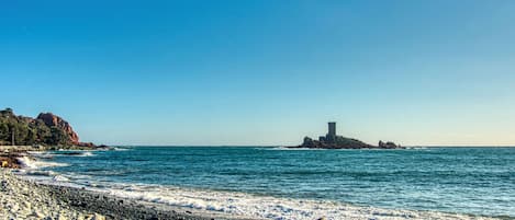 A rocky beach with a tower on a small island in the distance.