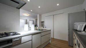 A modern kitchen with white cabinetry, a built-in oven, a dishwasher, and a refrigerator. - Araha Beachway Inn (Chatan)