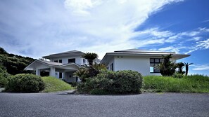 Stunning two-story building with a central entrance and two wings, each with a balcony, surrounded by lush greenery.