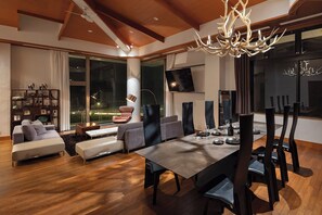 Een moderne woonkamer met een eethoek, houten vloeren en een grote kroonluchter.