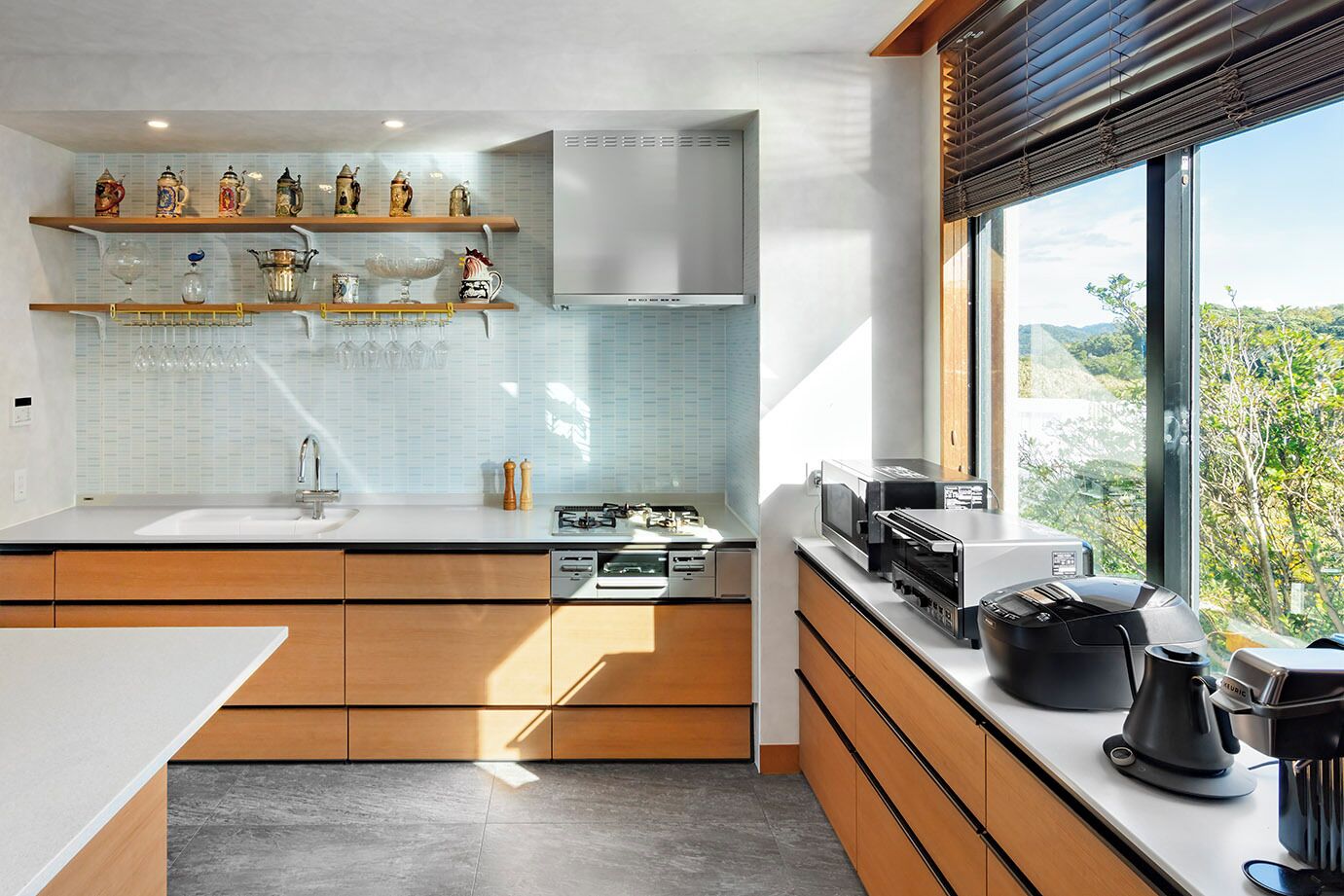 A modern kitchen with wooden cabinets, a white countertop, and a window with a view of greenery.