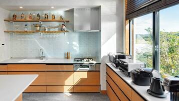 A modern kitchen with wooden cabinets, a white countertop, and a window with a view of greenery.
