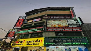 A multi-story building with various signs advertising services like A/C rooms, party hall, and wedding engagement reception. - Sundaram Residency (Chennai)