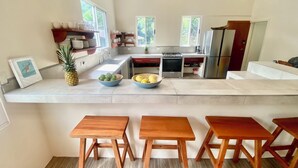 Une cuisine moderne avec un îlot central, des tabourets en bois et un réfrigérateur.