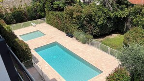 A rectangular swimming pool with a tiled deck, surrounded by lush greenery and a white fence. - Fully equipped studio in the center of Cannes with swimming pool, large terrace and air conditioning  (Cannes)