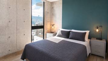 A bedroom with a large bed, two bedside tables, a view through a window, and a teal accent wall.