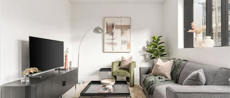 A modern living room with a flat-screen TV, a dark grey sofa, a coffee table, and a green armchair.