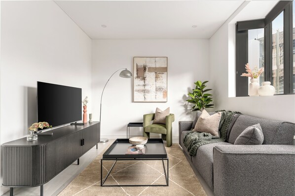 A modern living room with a flat-screen TV, a dark grey sofa, a coffee table, and a green armchair. - Pyrmont Apartments by Urban Rest (Pyrmont)