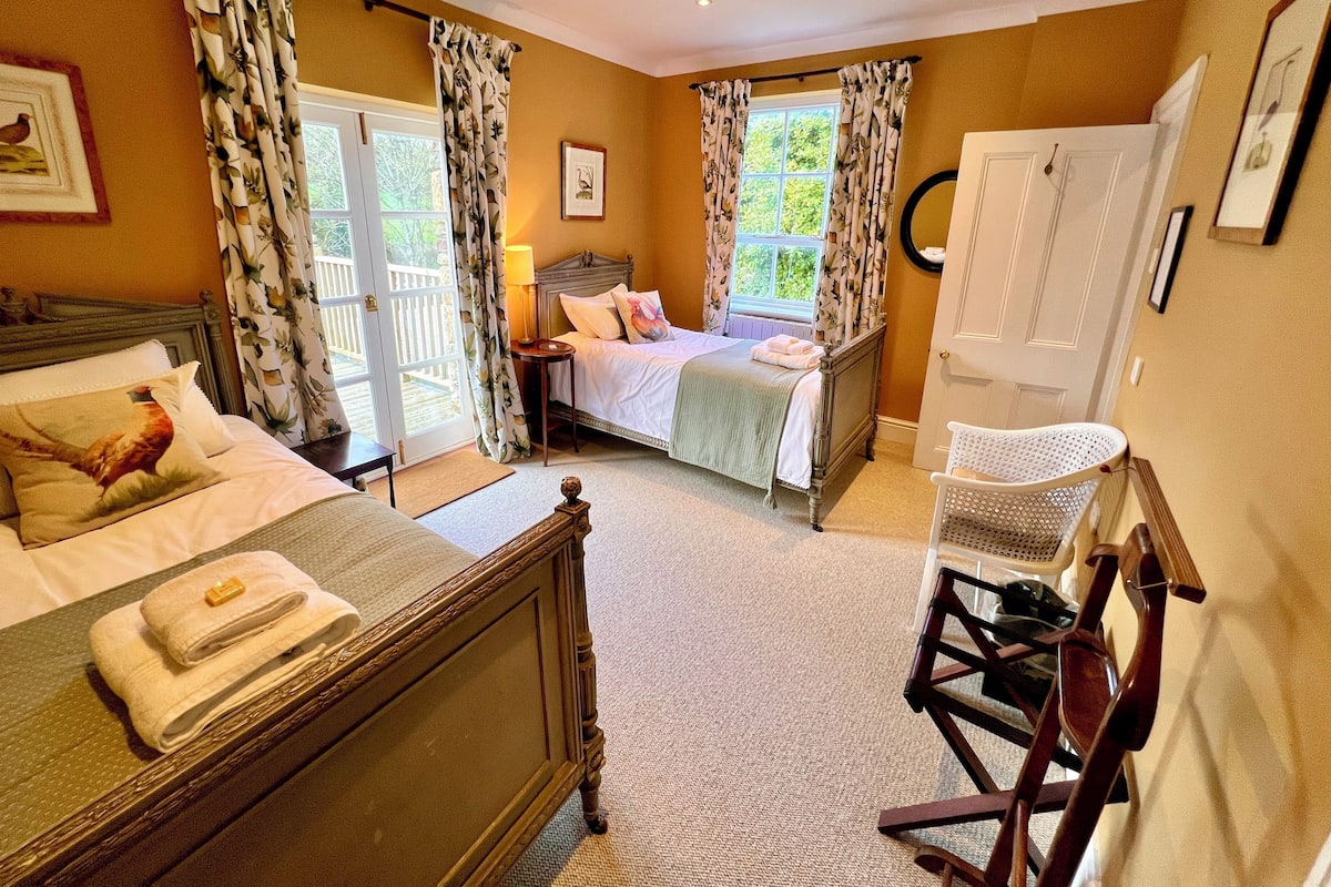 A bedroom with two beds, a wooden headboard, a nightstand, a chair, and a window with curtains.