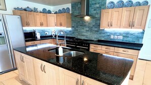 A kitchen with light wood cabinets, a black granite countertop, a stainless steel sink, and a built-in oven. - The Mill House (Ballasalla)