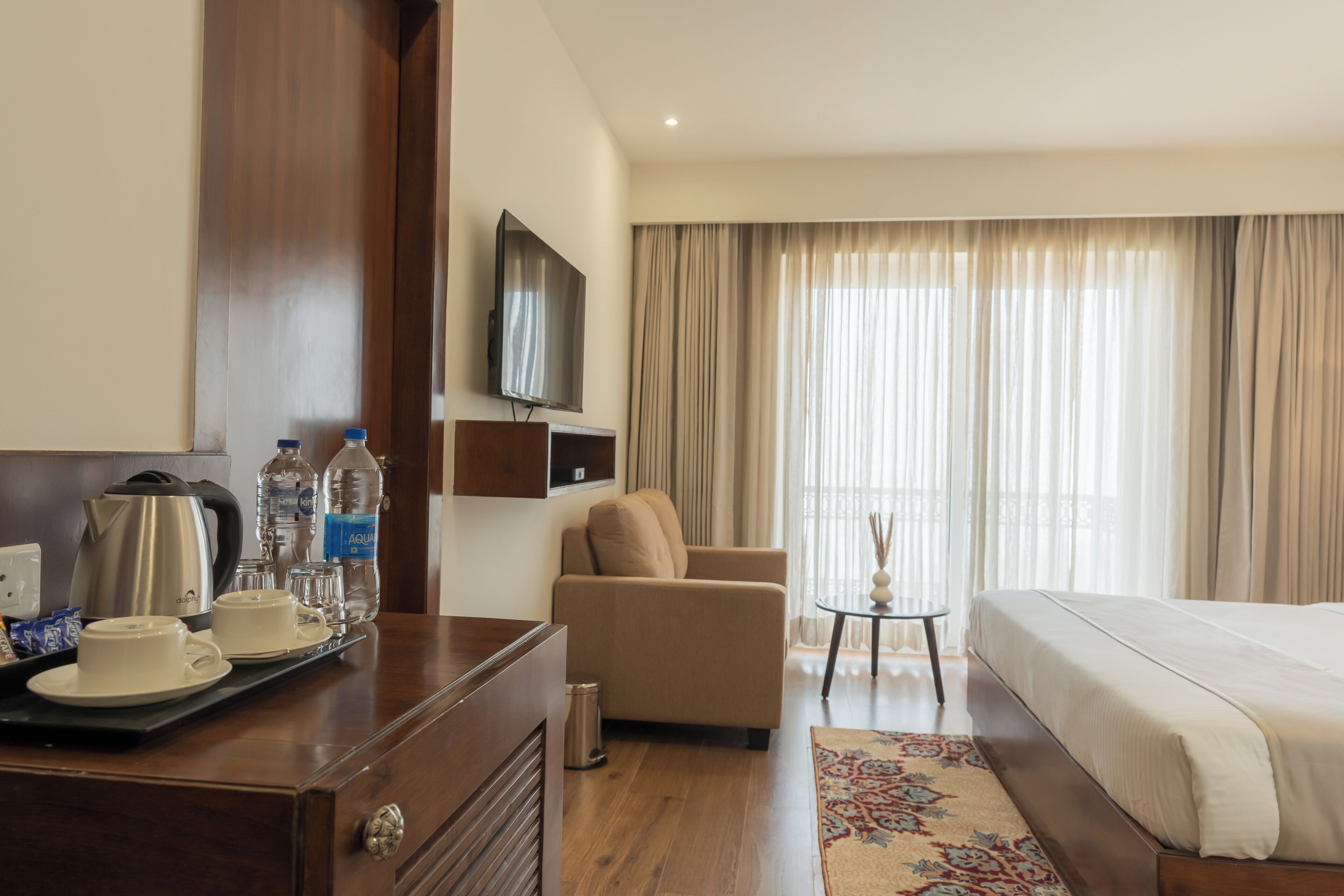 A hotel room with a bed, a sofa, a television, a coffee table, and a desk with a kettle and cups.