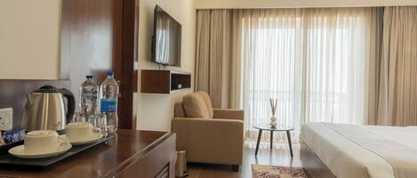 A hotel room with a bed, a sofa, a television, a coffee table, and a desk with a kettle and cups.