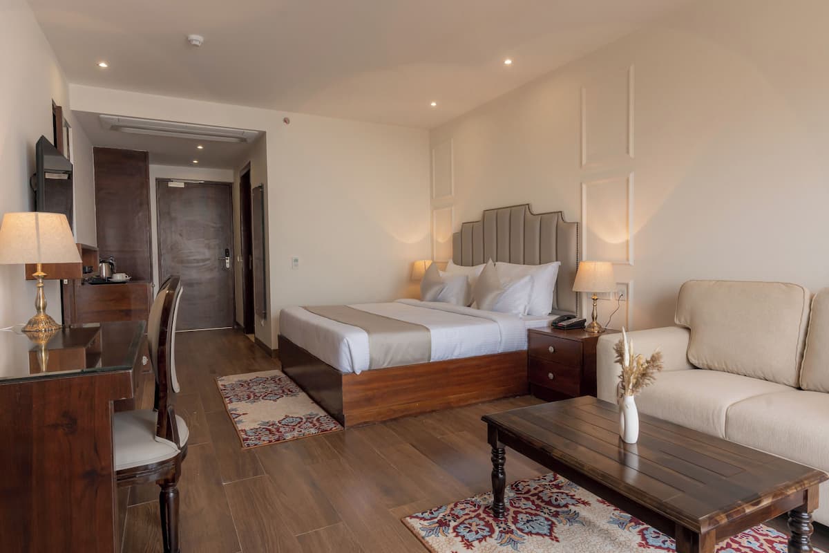 Een moderne hotelkamer met een houten bed, een bank, een bureau met lamp en een kleine tafel met vaas.