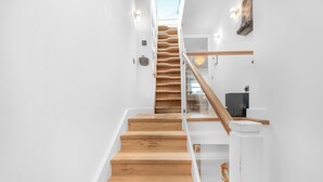 A staircase with wooden steps and glass railings, leading to a landing with a black object and a light fixture. - Family size Penthouse in Covent Garden w/roof garden & additional small patio (London)