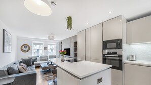 A modern kitchen with a central island, built-in appliances, and a dining area with a sofa and chairs. - Family size Penthouse in Covent Garden w/roof garden & additional small patio (London)
