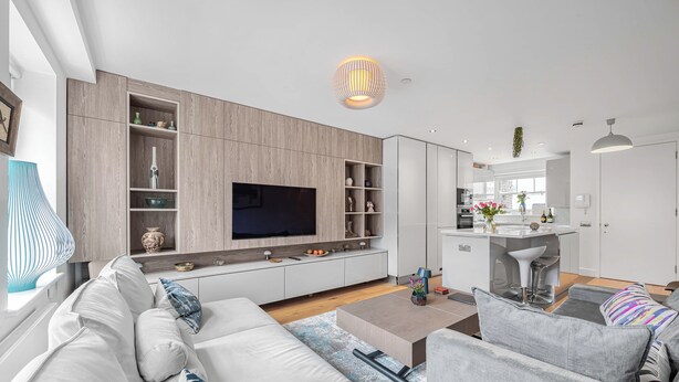 A modern living room with a large TV, built-in shelves, and a kitchen area in the background. - Family size Penthouse in Covent Garden w/roof garden & additional small patio (London)