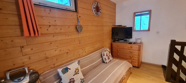 Puupaneloitu huone, jossa on sänky, televisio, kello ja ikkuna.