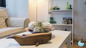 Un salon moderne avec un canapé blanc, une table d’appoint en bois surmontée d’un bol décoratif et une table basse blanche.