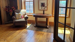 A cozy room with wooden flooring, a cushioned armchair, a small round table with a vase, and large windows offering a view of a building with a spire. - Stunning river view loft in Wabasha near Eagle Center (Wabasha)