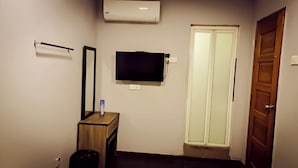 A small room with a wooden cabinet, a mirror, a flat-screen TV, a white door, and a trash bin. - Moon Night Hotel (Batu Caves)