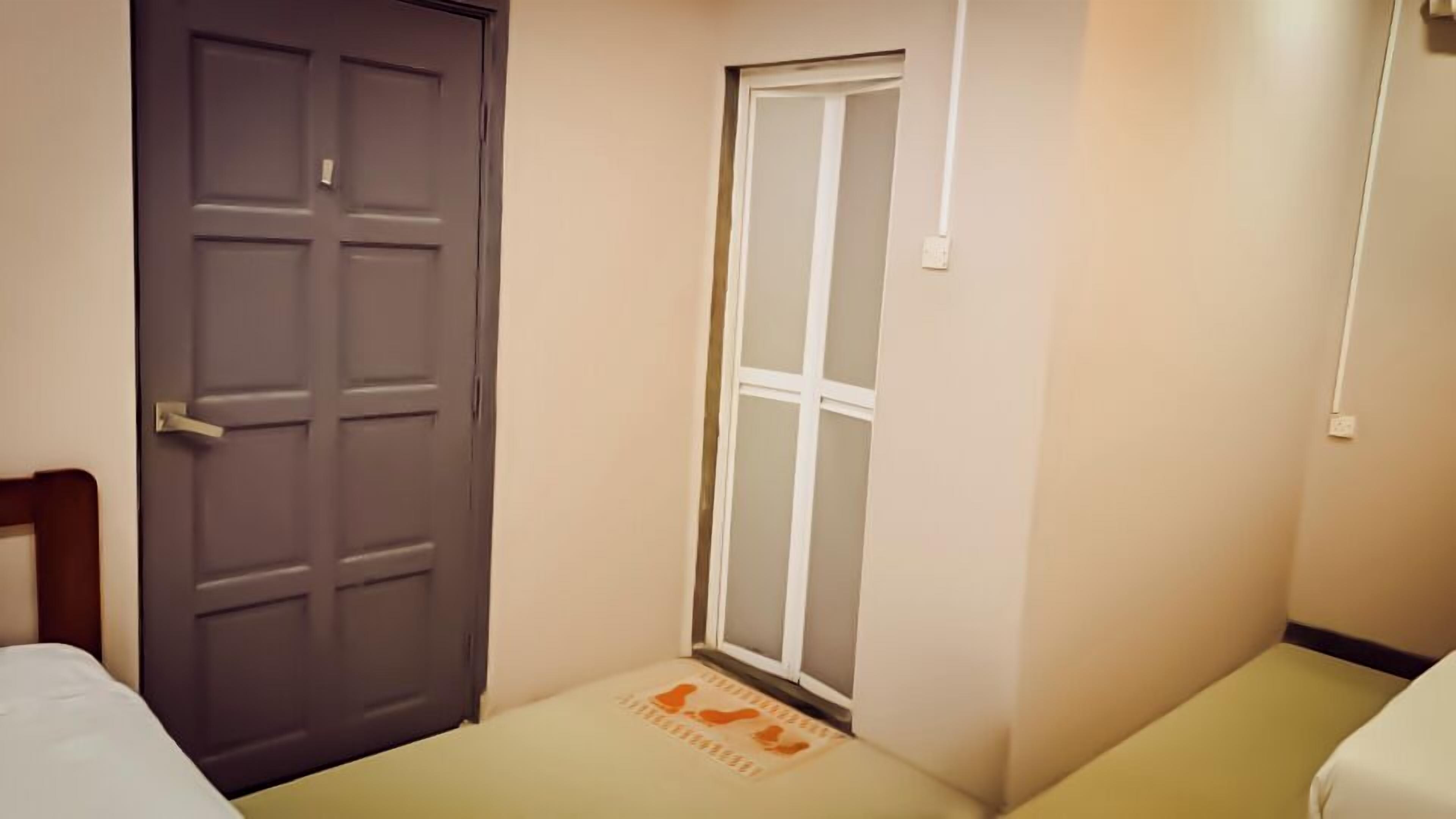 Um quarto pequeno e estreito, com uma porta, uma janela e uma cama.