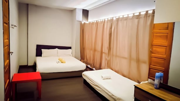 A hotel room with two beds, a red chair, a wooden nightstand, and beige curtains. - Moon Night Hotel (Batu Caves)