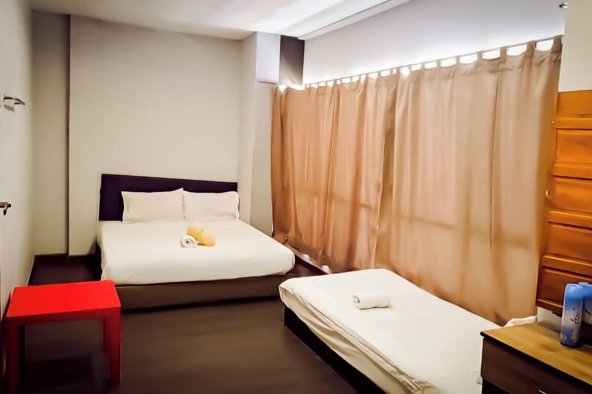 A hotel room with two beds, a red chair, a wooden nightstand, and beige curtains.