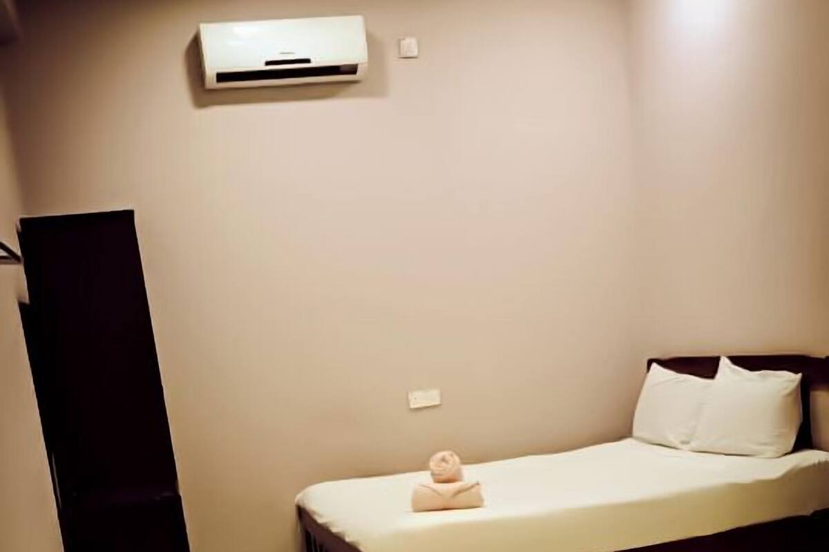 A hotel room with a single bed, a small table, and a dark-colored wardrobe.