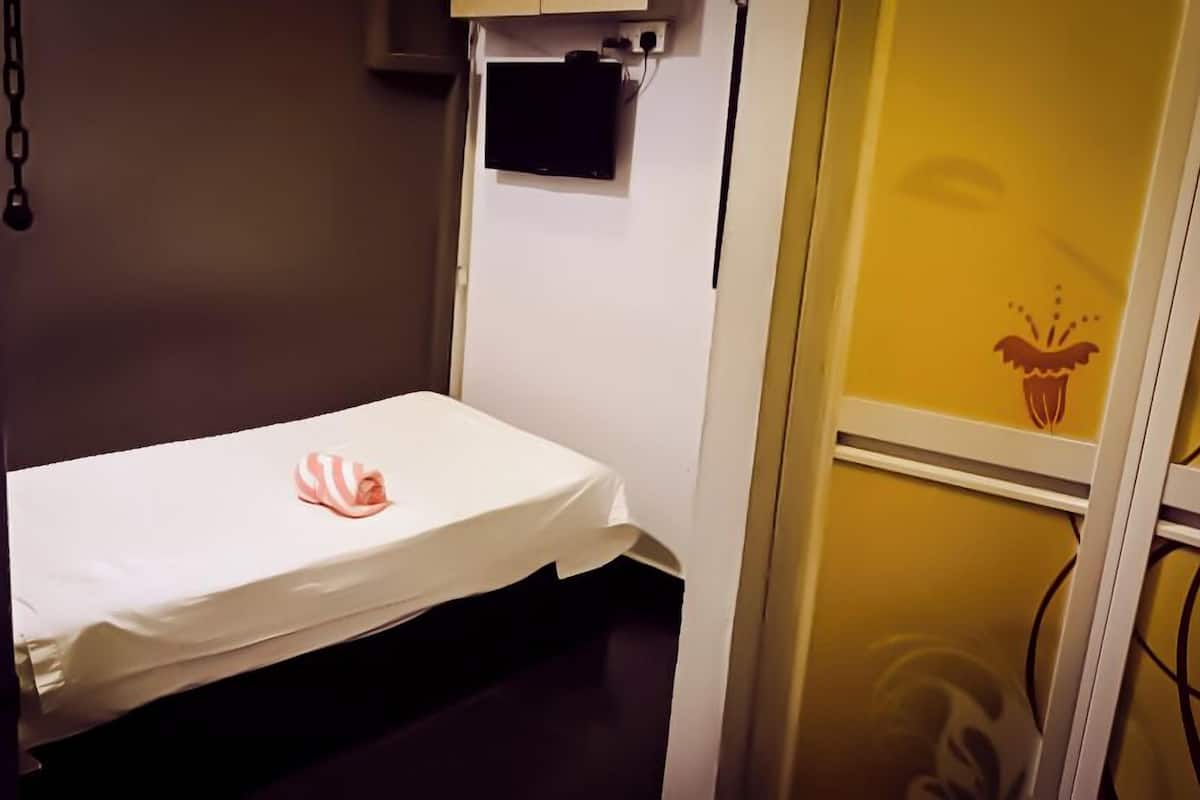 A small, single-bed room with a white bedspread and a pink and white striped towel.