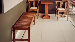 A small, modern room with a wooden bench, two wooden chairs, and a small table. - Moon Night Hotel (Batu Caves)