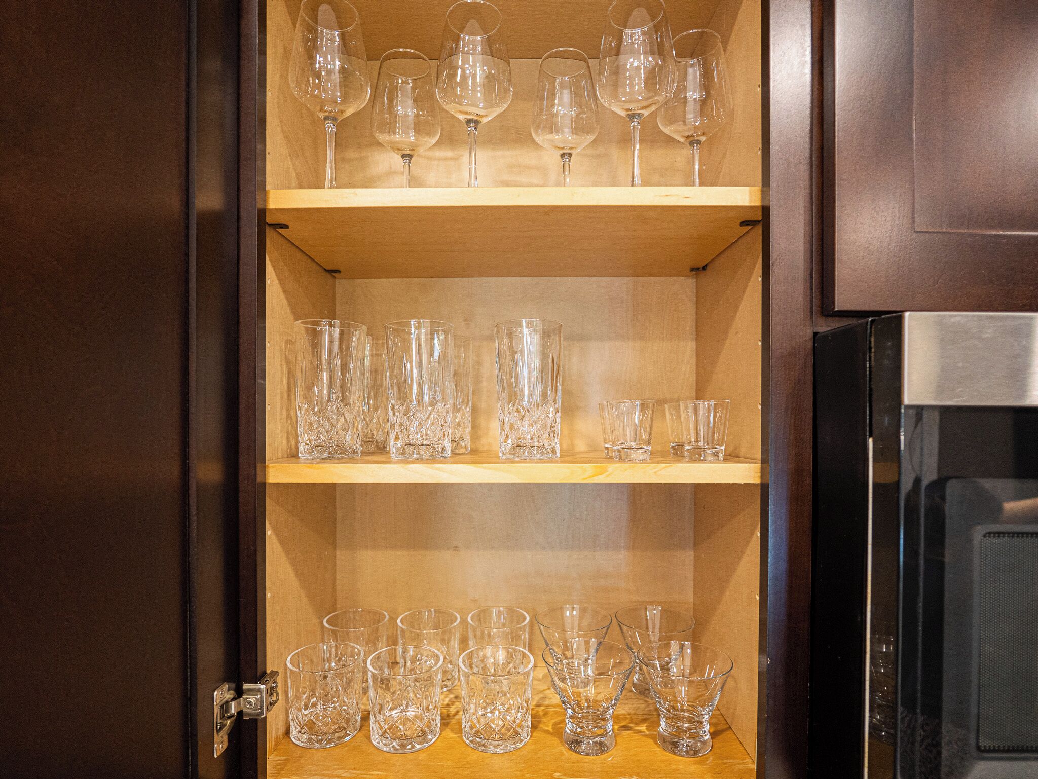 A cabinet with three shelves, each holding different types of glassware.