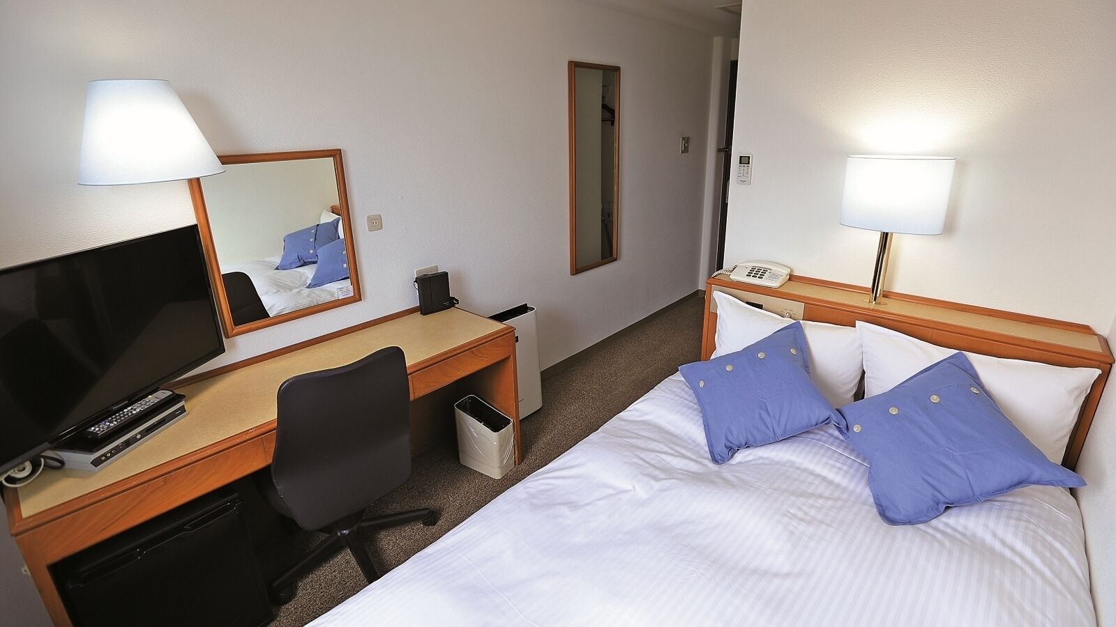 Hotellihuone, jossa on sänky, työpöytä tietokoneella, tuoli, televisio ja puhelin.