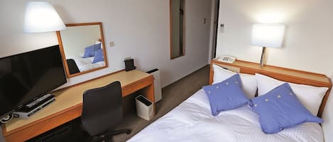 Een hotelkamer met een bed, een bureau met een computer, een stoel, een televisie en een telefoon.