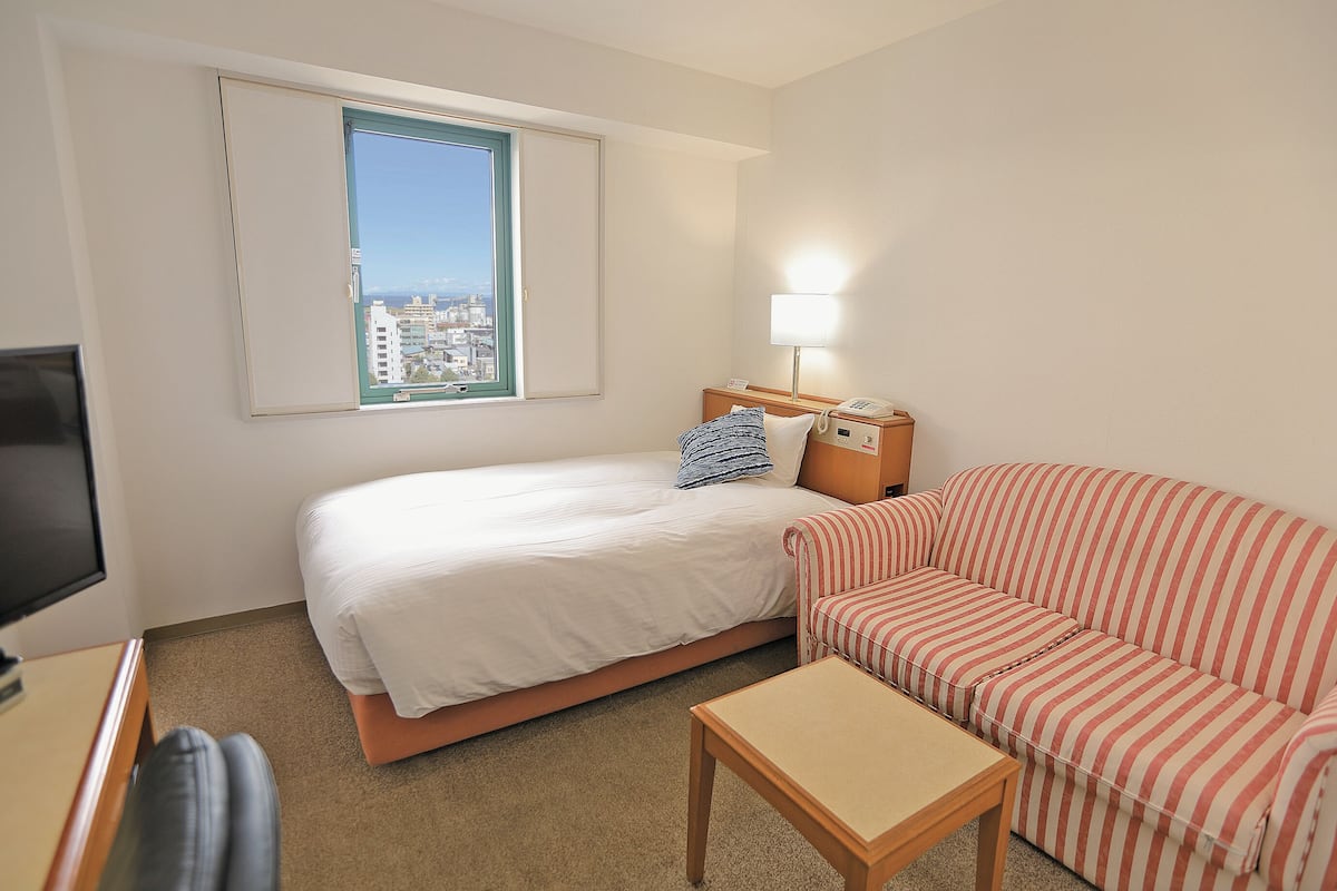 Una habitación de hotel con una cama, un sofá a rayas, una mesita, una lámpara y un televisor.