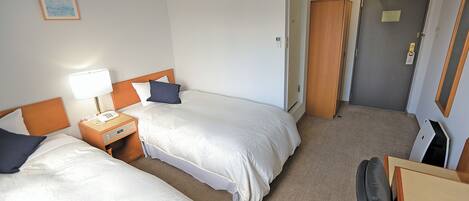 A hotel room with two beds, a bedside table with a lamp, a wooden headboard, and an air conditioning unit on the wall.