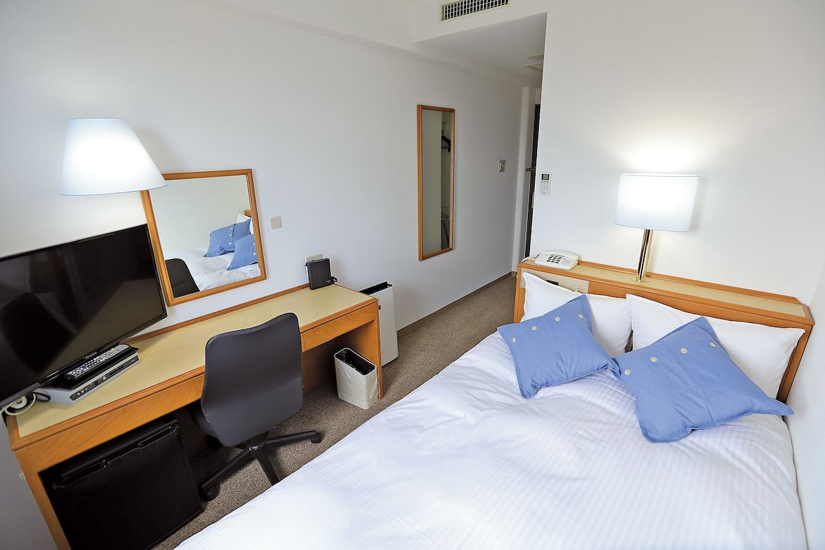 Una habitación de hotel con cama, escritorio, computadora, silla, televisor y espejo.