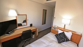 Habitación de hotel con cama, escritorio con televisor, silla, mesita de noche con lámpara y espejo.