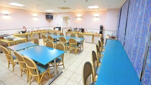 A dining area with multiple tables and chairs, a television on the wall, and a patterned curtain on the right. - Aomori Forest Hotel Annex (Aomori)