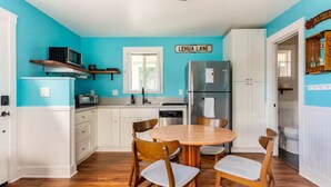 A kitchen with teal walls, white cabinetry, a stainless steel refrigerator, and a wooden dining table with chairs.