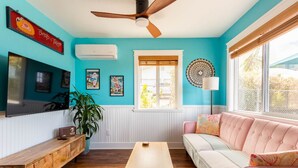 A room with teal walls, a ceiling fan, a wooden table, a pink sofa, and a window with blinds.