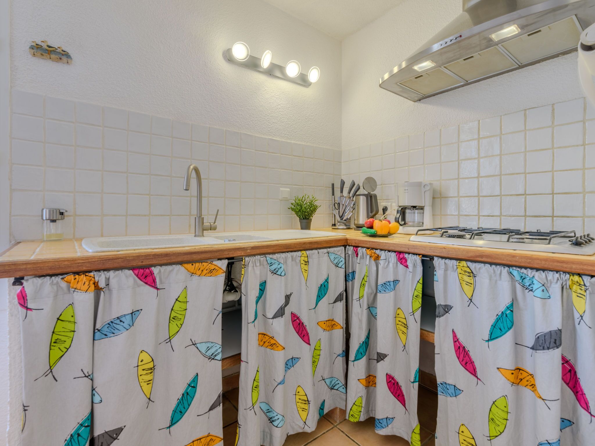 Eine Küche mit weißen Fliesen, einer Holz Arbeitsplatte, einer Spüle, einem Herd und einer Kaffeemaschine.