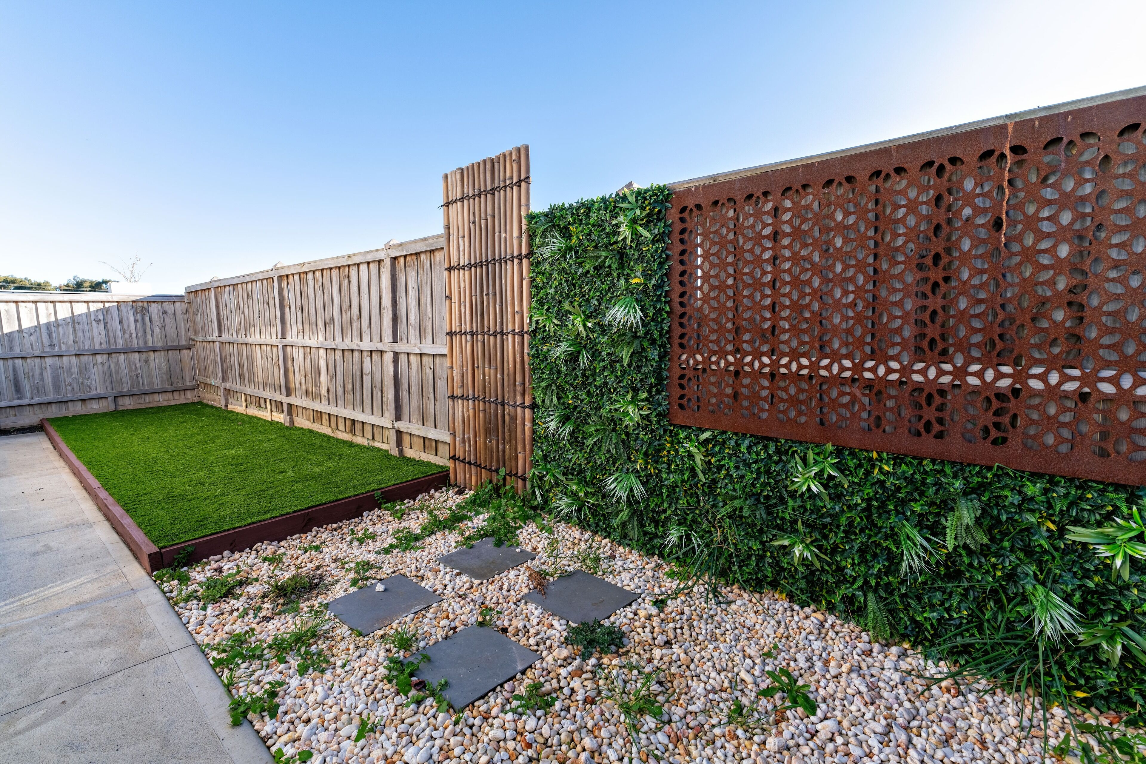 Un jardin avec une clôture en bois, une pelouse verdoyante, une clôture décorative en métal et un chemin de gravier.