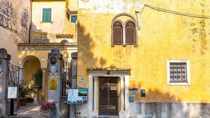 A yellow building with a central entrance, two arched doorways, and a small balcony with a flower pot.