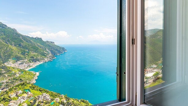 A coastal view from a window overlooking a turquoise sea and green hills.