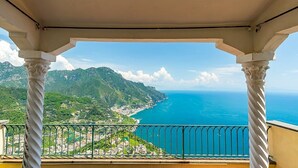 A balcony with a view of a coastal landscape, including a body of water and green hills.