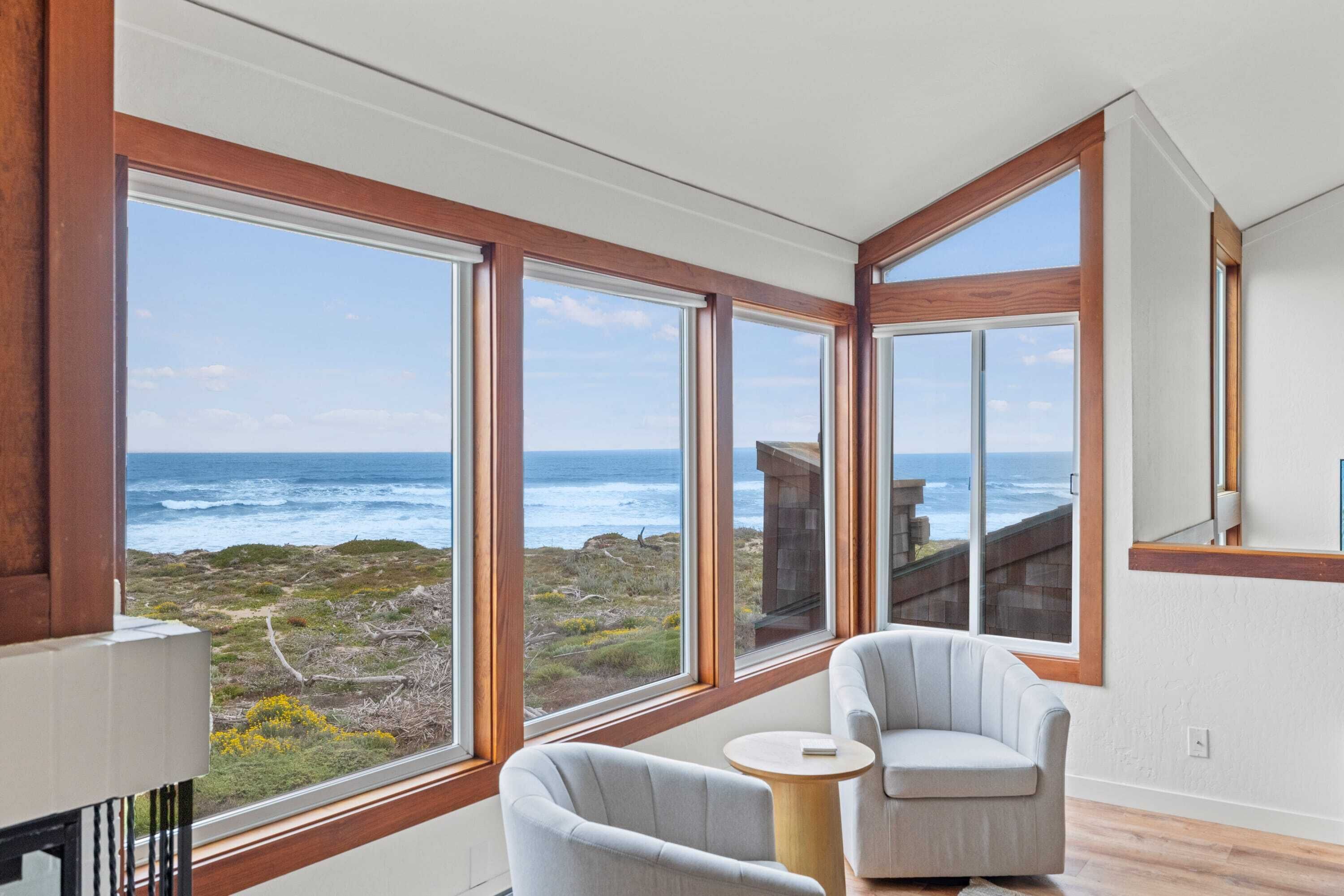 A room with large windows, a view of the ocean, and two chairs.